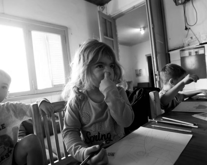 Three children drawing at a table in grayscale, indoors, natural light.