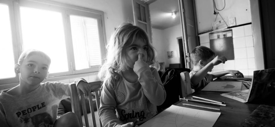 Three children drawing at a table in grayscale, indoors, natural light.