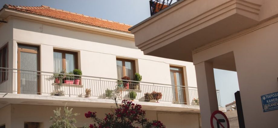 Traditional Greek house facade with potted plants and balcony details.
